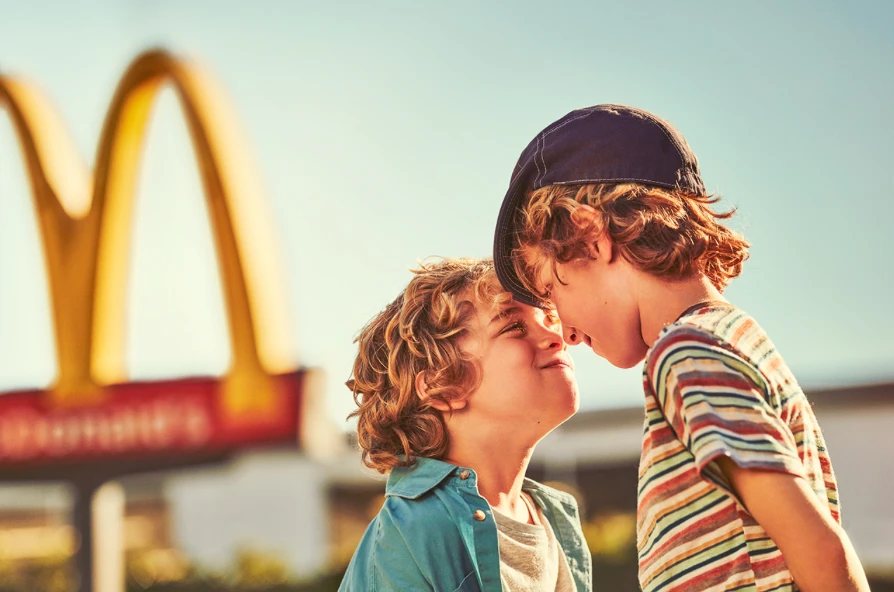 Two kids grinning at each other in front of the Golden Arches